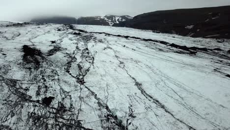 Aerial-landscape-view-of-Sólheimajökull-glacier,-Iceland,-melting-into-water,-in-summer,-with-people-hiking