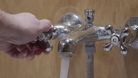 la mano enciende el agua caliente para el baño y verifica la temperatura