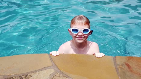 Young-Caucasian-boy-age-10-coming-out-of-the-water-in-a-pool-in-slow-motion-with-goggles-and-smiling