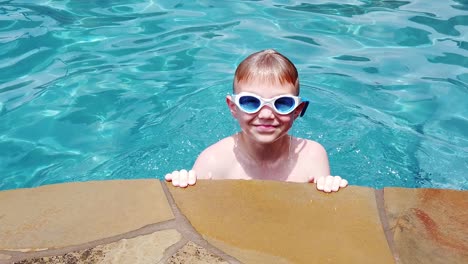joven caucásico de 10 años saliendo del agua en una piscina a cámara lenta con gafas y sonriendo
