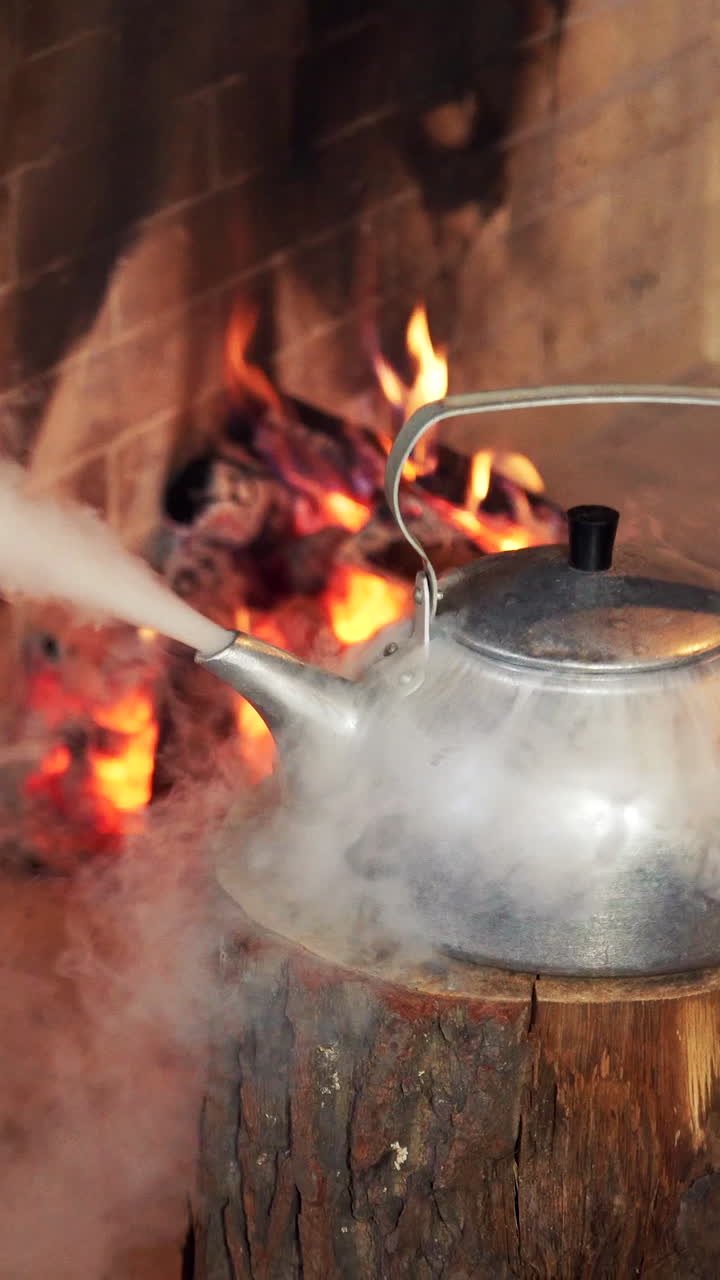 A steaming kettle by a fireplace, with a gloved hand adjusting it