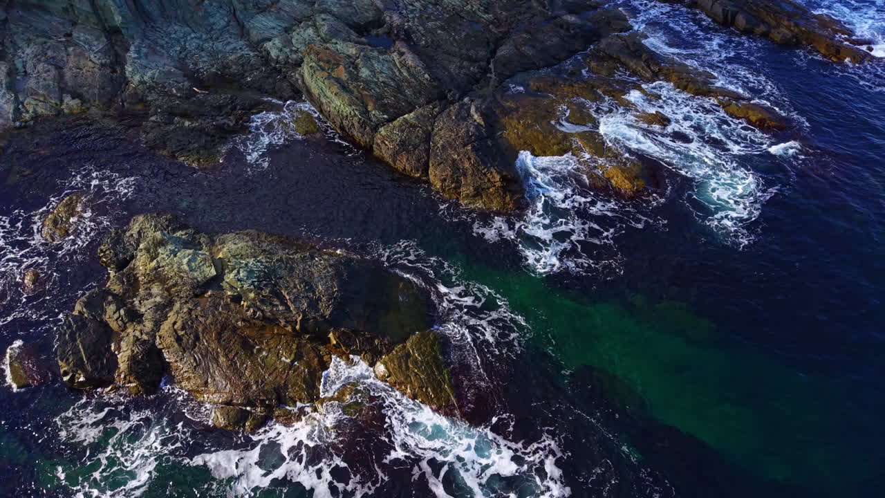 Le onde si infrangono contro le rocce frastagliate sotto un sole splendente in una tranquilla scena costiera piena di vita e colore