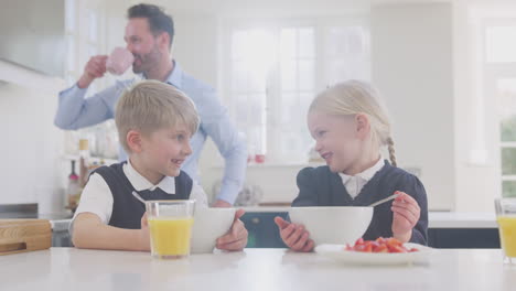 zwei kinder in schuluniform in der küche frühstücken, während sich der vater für die arbeit vorbereitet