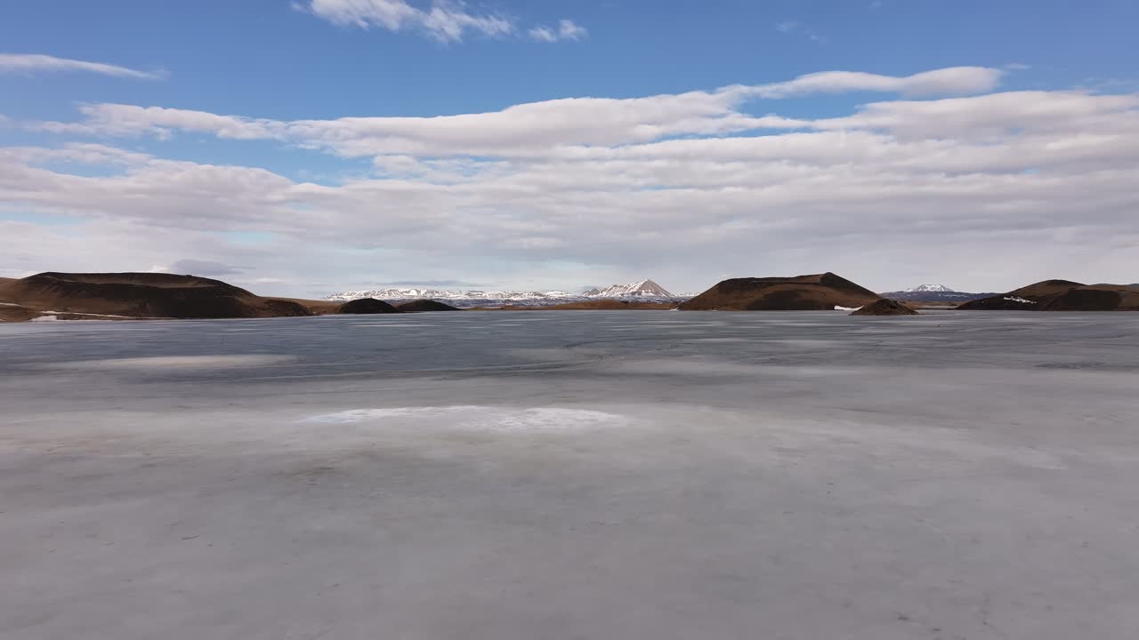 Aerial view of frozen Lake Mývatn near Reykjahlíð, Iceland, snow patches, volcanic hills and clouds.