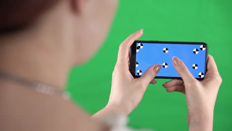 woman is zooming content in smartphone with tracking markers on display and green screen