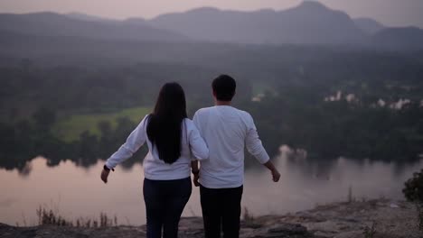 Una-Hermosa-Pareja-Vestida-De-Blanco-Tomando-Un-Largo-Respiro-Cerca-De-Un-Lago-Y-Una-Cordillera-Al-Atardecer