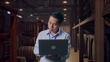 asian male professional worker standing with his laptop in cellar of winery, he is nodding his head with dissapionted