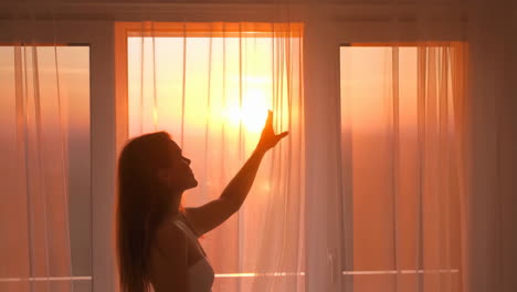 woman opening curtains at sunrise