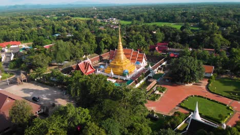 4k aerial drone shot - thai buddhist temple on sunny day, golden pagoda surrounding by green trees and bushes, orange roof tile, thai buddhism wat, religion believe meditation, peaceful calm scenic