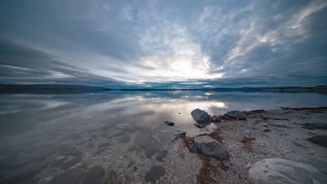 storm clouds move quickly above the calm fjord and pebble beach, captured in a timelapse video