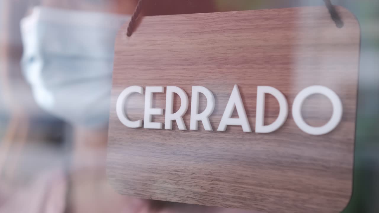 Unrecognizable woman with face mask changing closed to open sign in spanish. Start-up at covid time concept.