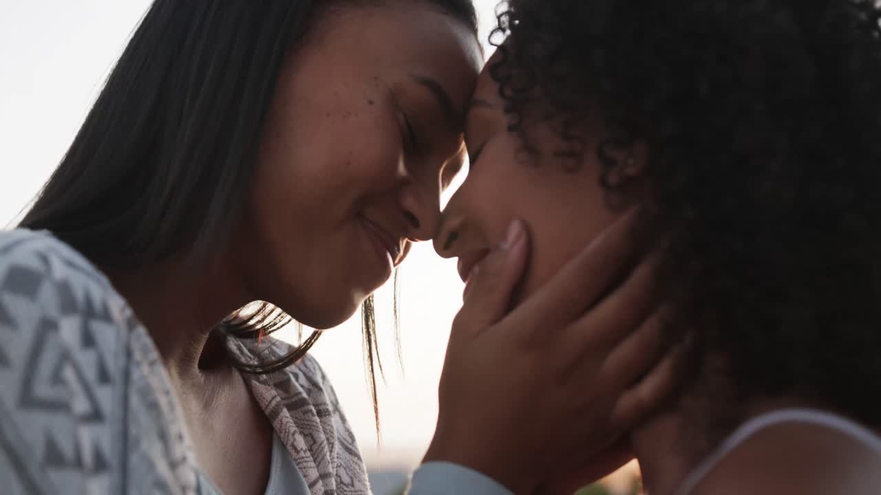 Romantica coppia lesbica birazziale che sorride e si abbraccia in giardino al tramonto, al rallentatore