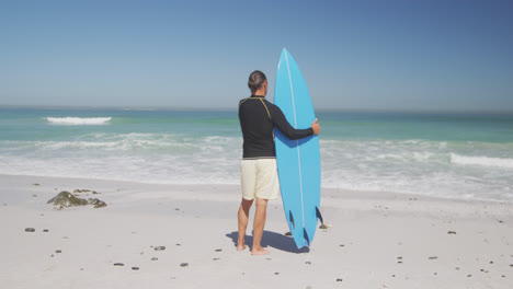 Hombre-Caucásico-Mayor-Sosteniendo-Una-Tabla-De-Surf-En-La-Playa