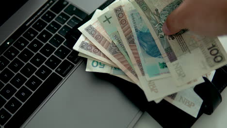 man put polish banknotes with black wallet on laptop, polish money and national currency