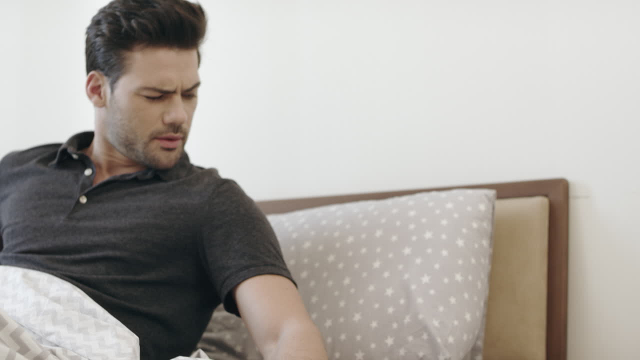 잠든 남자가 아침에 침실에서 깨어난다. 예쁜 남자가 알람 시계를 끄고 있다.