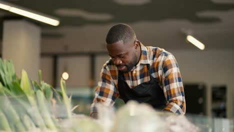 portrait of a black-skinned man in a plaid shirt and black apron sorting vegetables on a supermarket counter