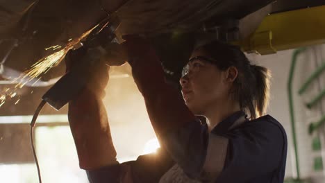 female mechanic using electric blade cutter and working under a car at a car service station