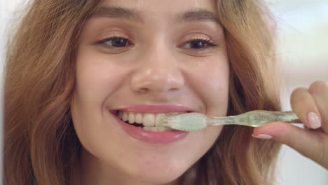 Mujer-Sonriente-Cepillando-Los-Dientes-Con-El-Espejo-Frontal-Del-Cepillo-En-El-Baño-De-Casa