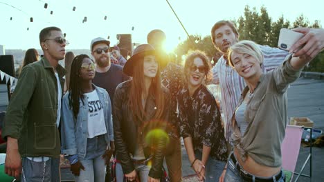 Cheerful-Young-Multiethnic-People-Having-Fun-And-Laughing-While-Posing-To-The-Smartphone-Camera-And-Taking-Selfie-At-The-Rooftop-Party