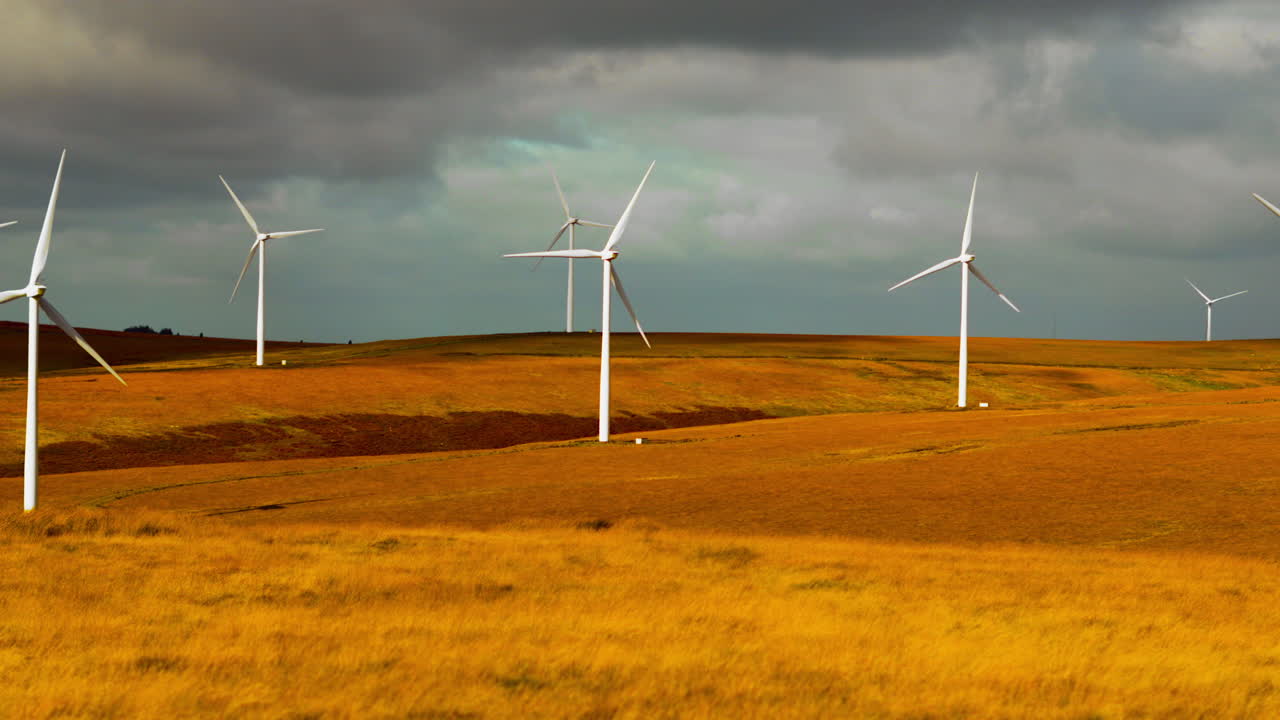 Slow Pan Across Fast Rotating Wind Farm in Wales with Dark Storm Clouds Forming Above with Rich Colorful Moorland Landscape. Clean Renewable Energy Generated in Natural Countryside in Wales, UK