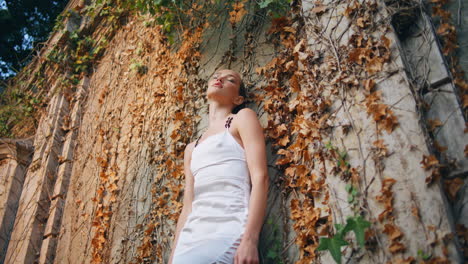 mujer relajada inclinada edificio medieval cubierto de follaje de otoño. modelo posando