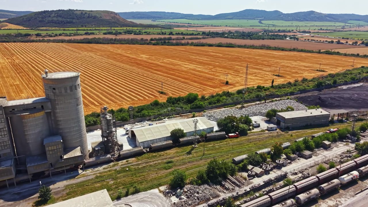 View of industrial area and farmland in rural setting during daytime near a small town surrounded by hills and fields