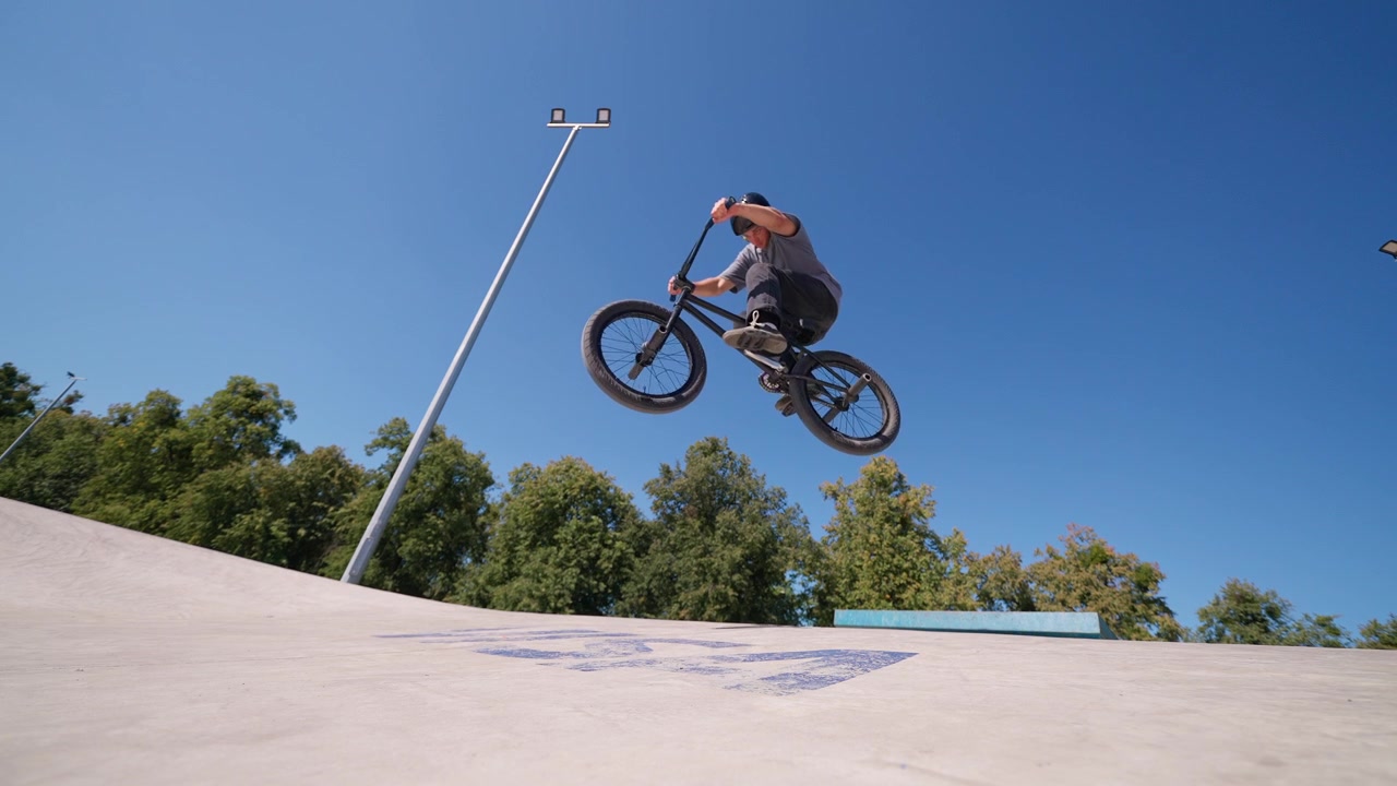 Giovane uomo che esegue un salto in BMX in uno skatepark soleggiato
