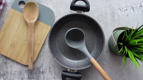 kitchen still life with a pan, wooden spoon, cutting board, and a plant