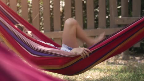 young happy little girls in summer camp lying in colorful hammocks relaxing playing outside with plushes dog dolls in green grass field kids children slow motion