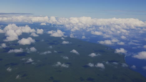 Una-Impresionante-Vista-Aérea-Desde-Un-Avión-Muestra-Una-Exuberante-Isla-De-Bosque-Tropical-Rodeada-De-Vastas-Nubes-Esponjosas-En-El-Cielo