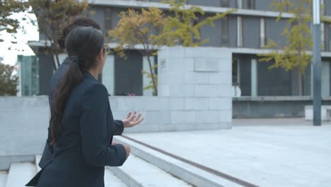 Two-confident-business-women-talking-together-while-walking-near-office-building