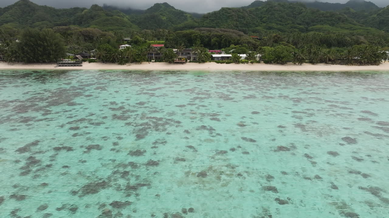 Luftoptagelse, der bevæger sig mod venstre, af et kystnært koralrev, der beskytter farvandet i Rarotonga, Cookøerne, et tropisk paradis.