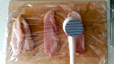 ablandamiento del lomo de cerdo con un martillo de carne de madera a través de una película adhesiva sobre una tabla de cortar de madera, slomo superior