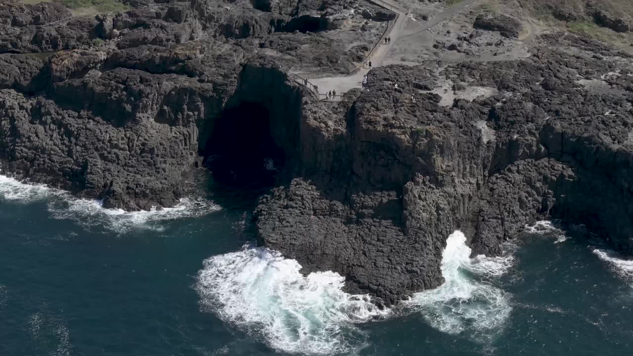 la órbita aérea muestra una escarpa rocosa expuesta cayendo al océano a medida que el agua drena a través de las grietas en kiama, nsw, australia.
