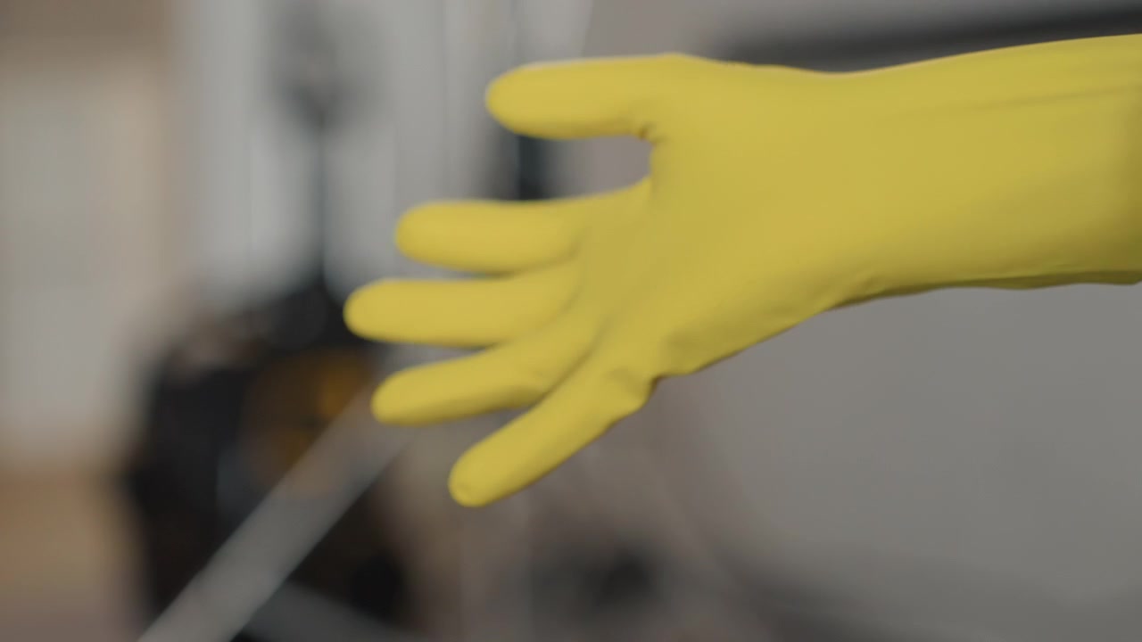 Mujer blanca poniéndose guantes amarillos, primer plano de manos alisando los dedos y ajustando un anillo, fondo de estudio borroso, preparándose para una limpieza profunda, rutina de protección, luz de la tarde