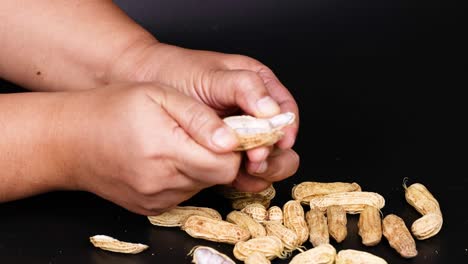 manos pelando cacahuetes sobre un fondo negro