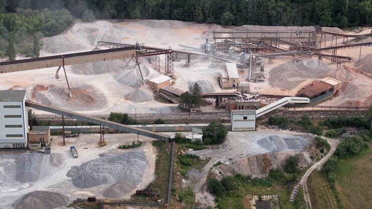 Aerial view of an active quarry, showcasing industrial machinery processing gravel and sand with conveyor belts and stockpiles.