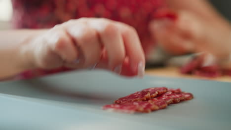 chef hands delicately layering thin cured meat slices on flat slate plate, creating stylish foodie presentation with vibrant red marbling and precise placement under soft natural window light