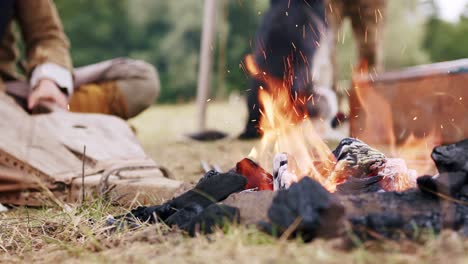 static close-up of a person dressed in medieval costume applying bellows to campfire in slow motion