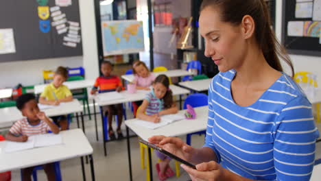 vista lateral de una maestra caucásica usando una tableta digital en el aula 4k