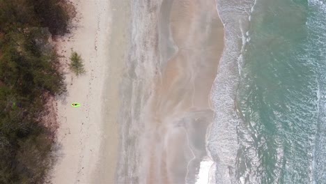 Aerial-top-down-view-of-a-man-laying-on-lamzac-on-a-sandy-beach-with-a-forest-behind