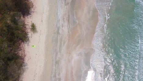 aerial top down view of a man laying on lamzac on a sandy beach with a forest behind