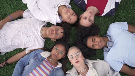 relaxed teenager friends lying together on green grass with eyes closed, dreaming and sleeping