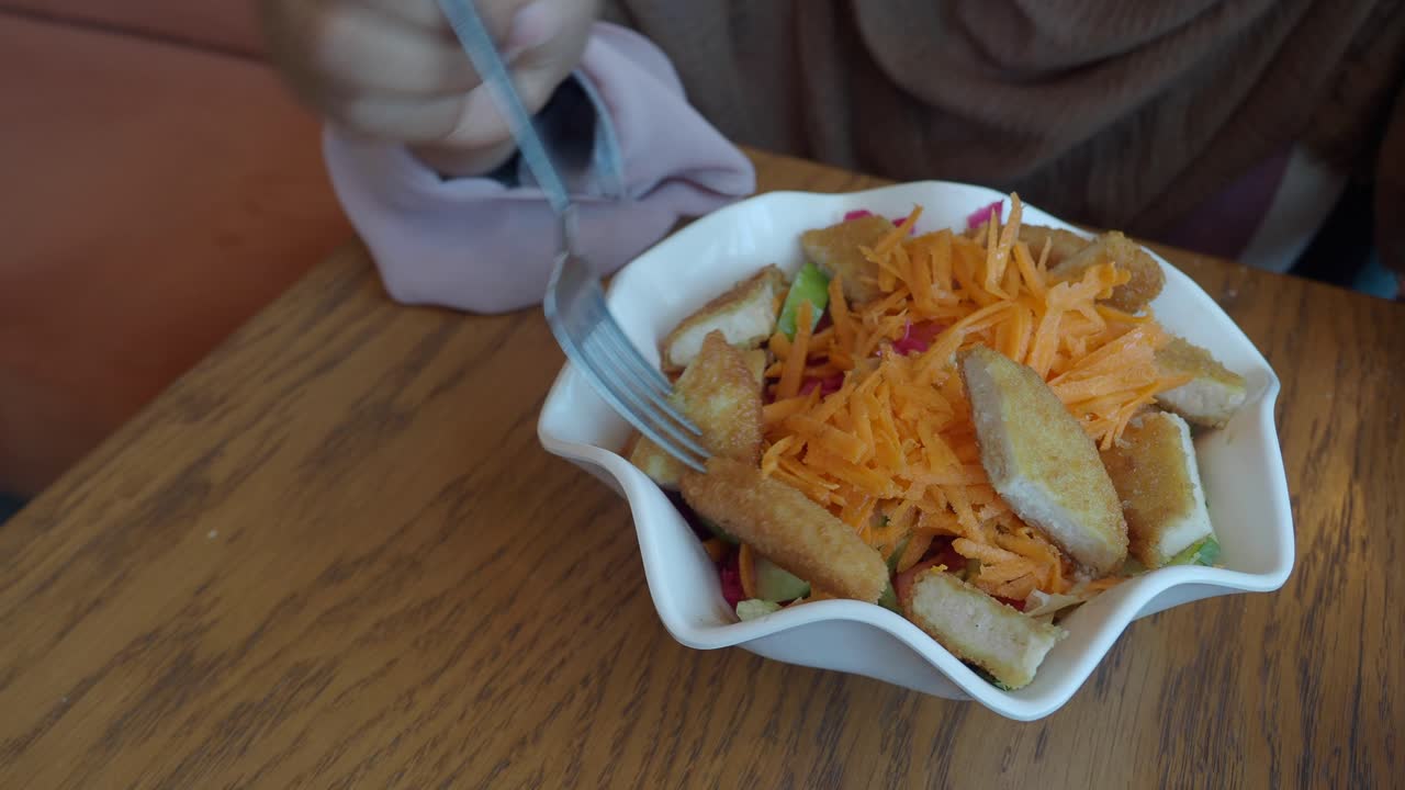 Close-up of a person eating a salad with fried chicken and vegetables