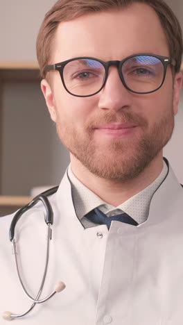 a young intern doctor in a white coat is looking at the camera and smiling.
