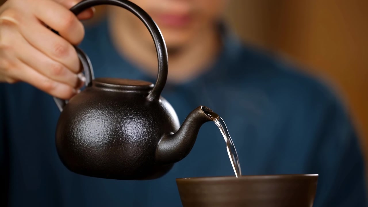 Primo piano di una persona che versa il tè dalla teiera nella tazza, interno caldo, ciotola di ceramica, vapore che sale, mano ferma