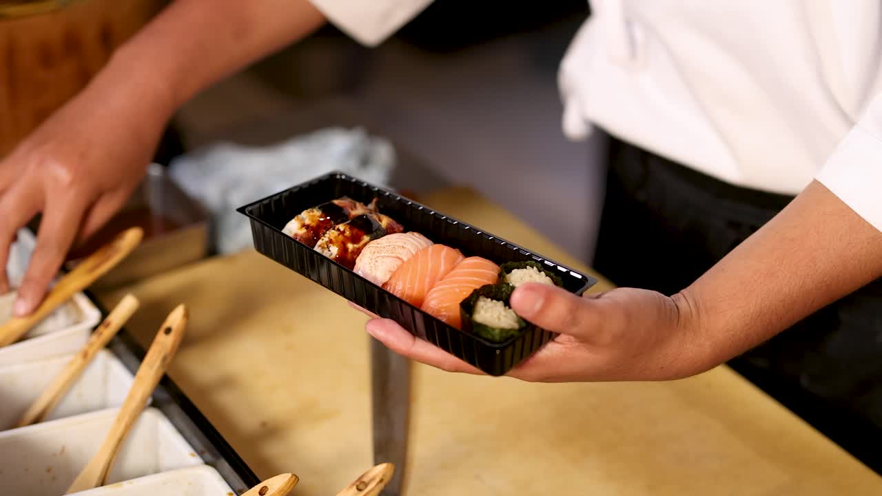 Uno chef di sushi professionista spennella accuratamente la salsa agrodolce su salmone e anguilla in un contenitore da asporto