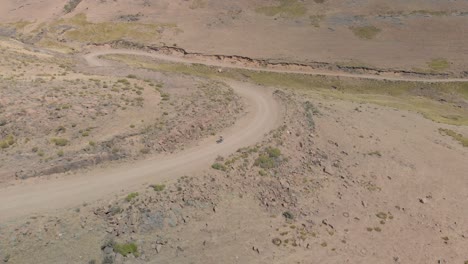 Toma-Aérea-Siguiendo-A-Un-Ciclista-De-Montaña-Subiendo-Un-Paso-En-Un-Camino-De-Grava