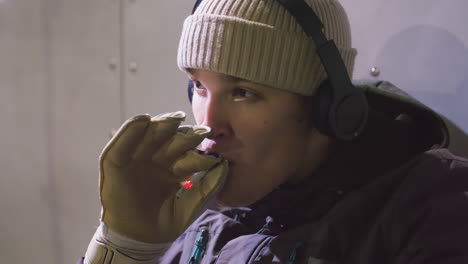 primer plano de un atleta con chaqueta de invierno con auriculares y guantes fumando al aire libre con una expresión enfocada e introspectiva