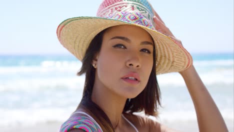 Mujer-Joven-Sonriente-Sosteniendo-Su-Sombrero-Para-El-Sol